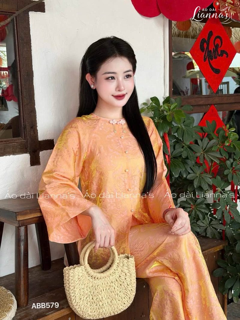Áo bà ba gấm màu cam tay loe, cổ tròn với nút thắt kiểu xưa, phối túi cói