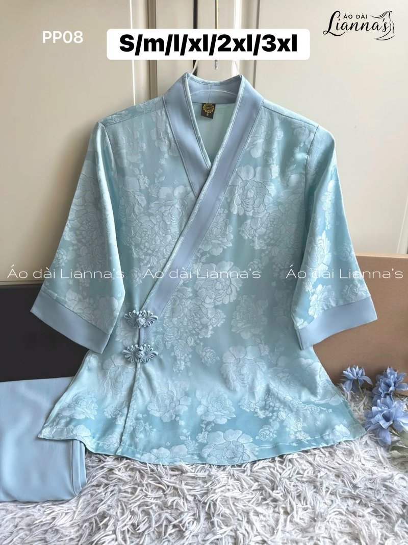Áo pháp phục xanh lam nhạt cổ chéo vạt, mặt vải hoa văn chìm, cài nút thắt bên hông